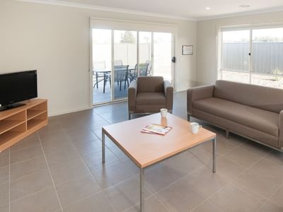 Living room with couch, coffee table, TV, and patio at La Trobe University Regional Housing – Shepparton.