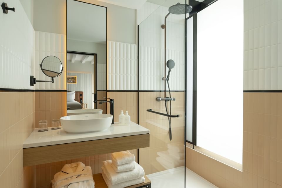 Bathroom featuring a vessel sink on a wooden vanity by a glass walk-in shower in the guest room at Urban Hive Madrid