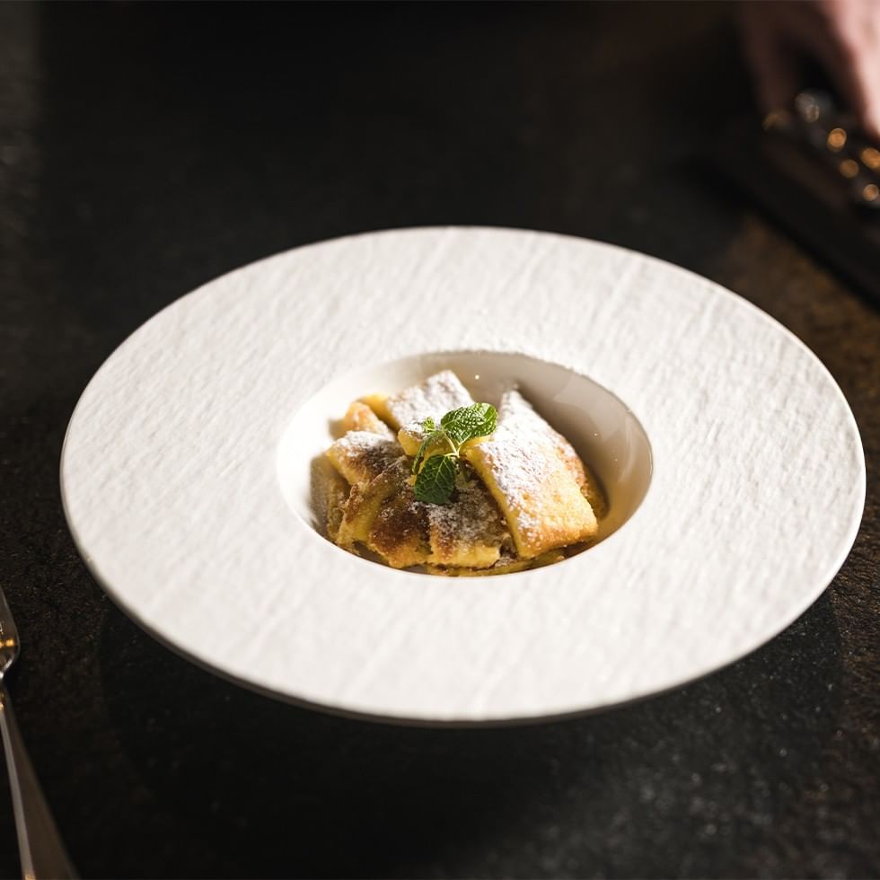 Dessert plate with pastry, mint, and powdered sugar on a table with a fork.