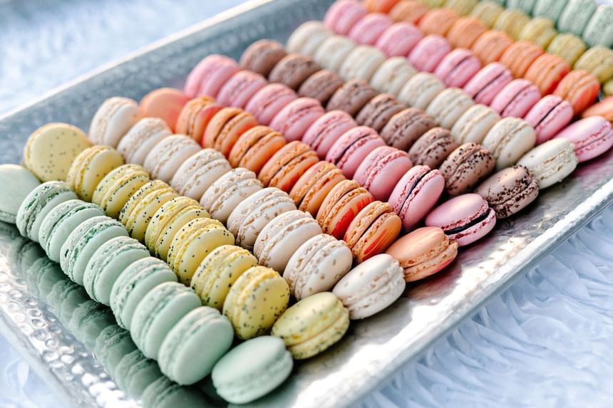 A vibrant display of colorful gourmet macarons arranged in neat rows on a silver tray at The White House Hotel