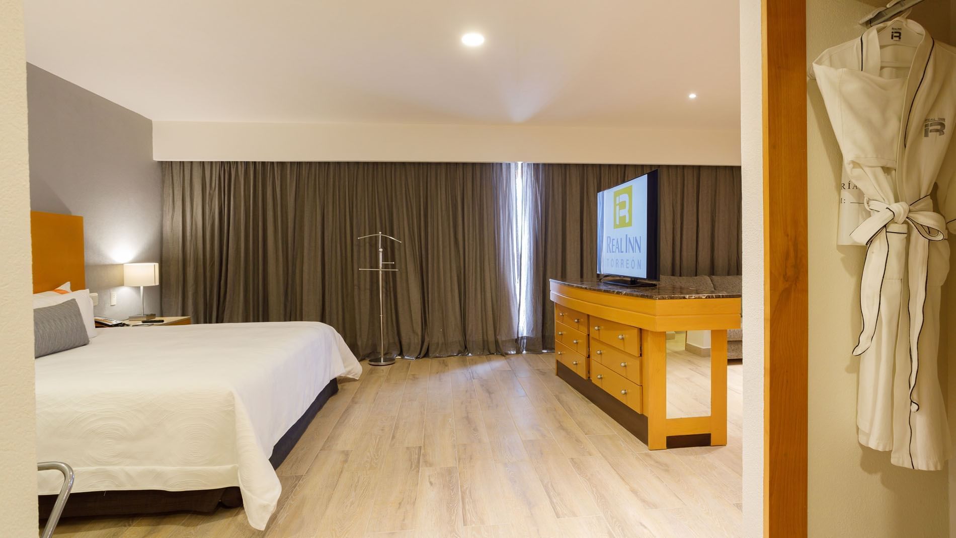 King Master Suite with a large wooden TV stand, light floors, and neutral grey drapes at Real Inn Torreon