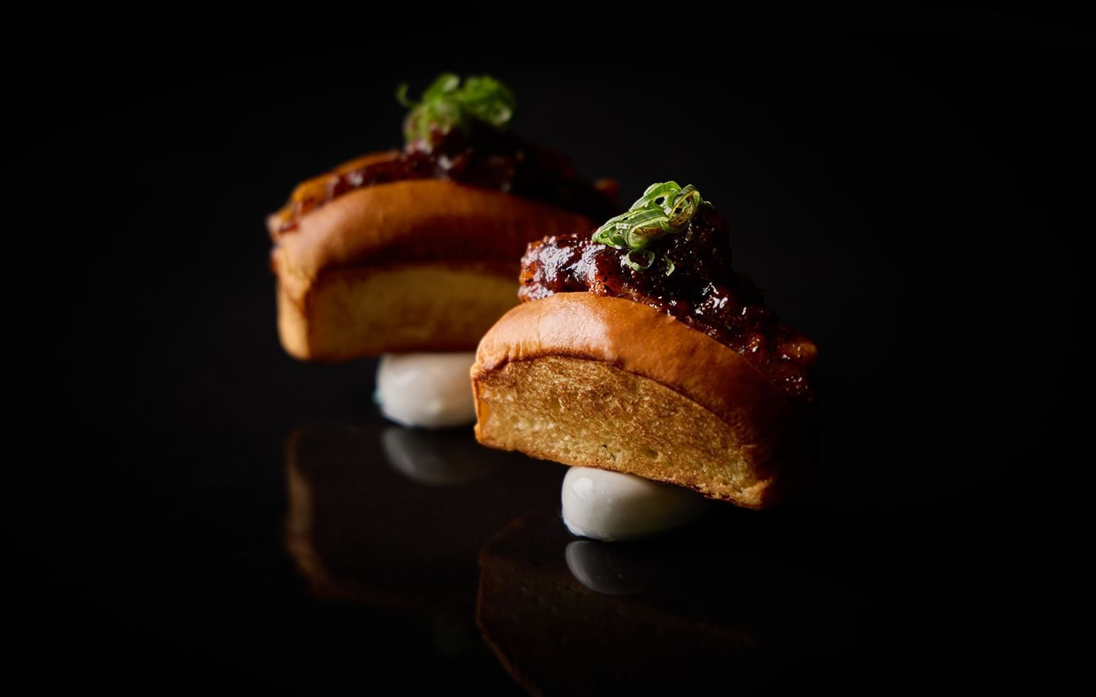Two savory brioche rolls with a sticky ginger glaze and green garnish, part of the food menu at 8 at the Londoner 