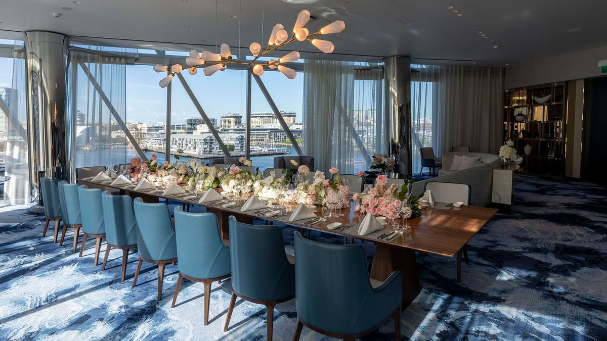 Long dining table, chairs and large windows offering ample natural light in wedding hall at Crown Towers Sydney