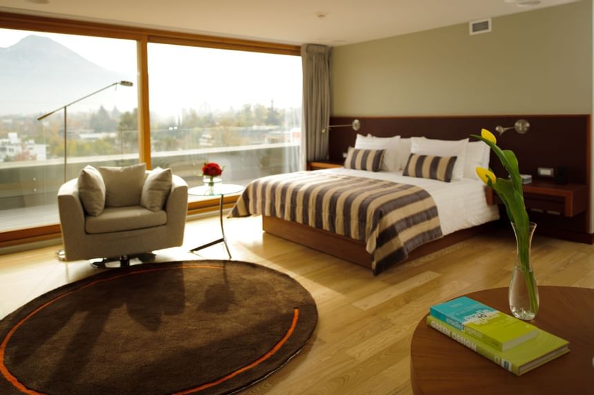 Cama listrada junto a sofá sob luz quente perto de janela grande com vista para montanhas na Terrace Suite no NOI Vitacura