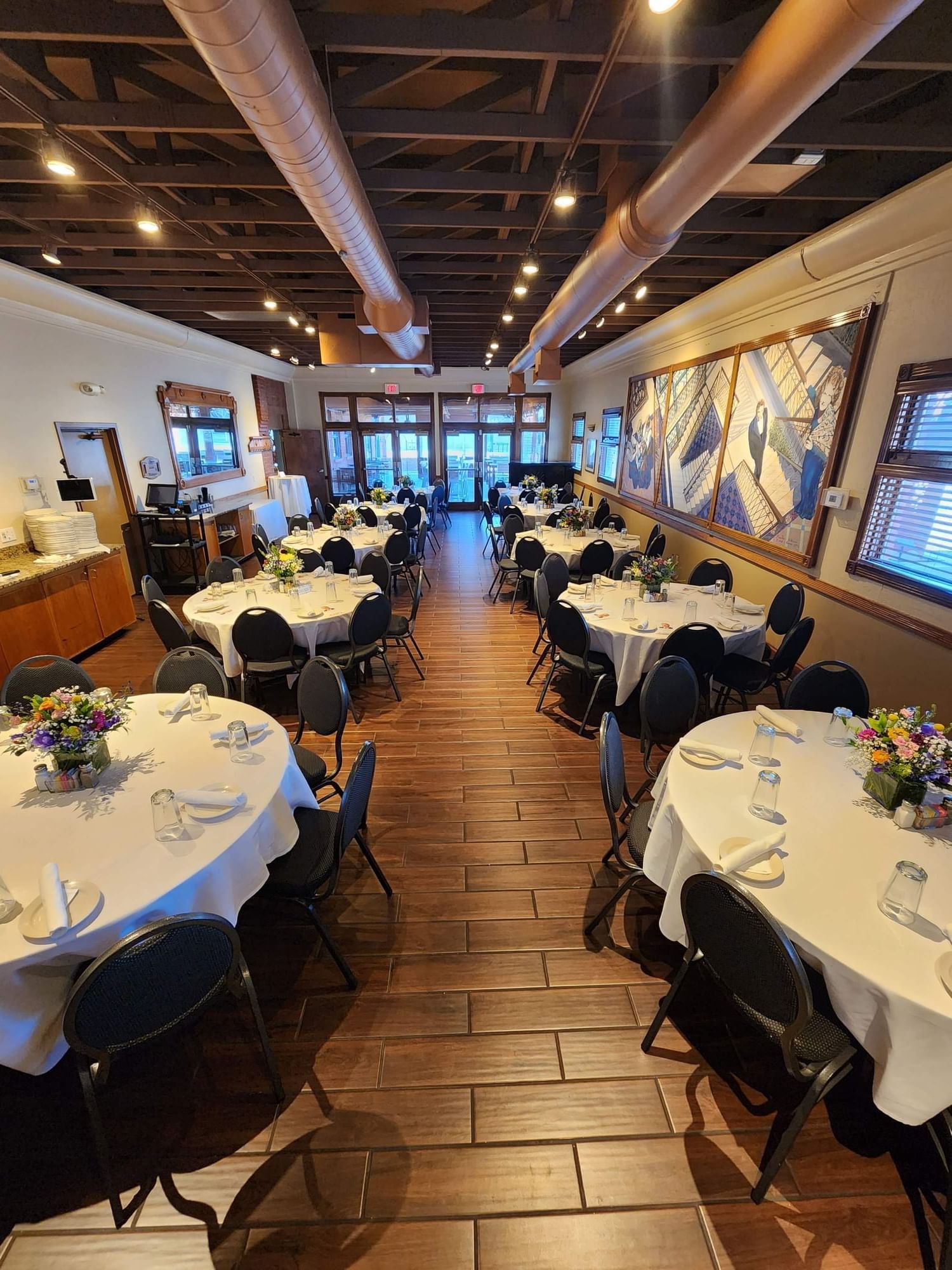 A dining area with round tables set with white tablecloths, black chairs, and flower centerpieces.