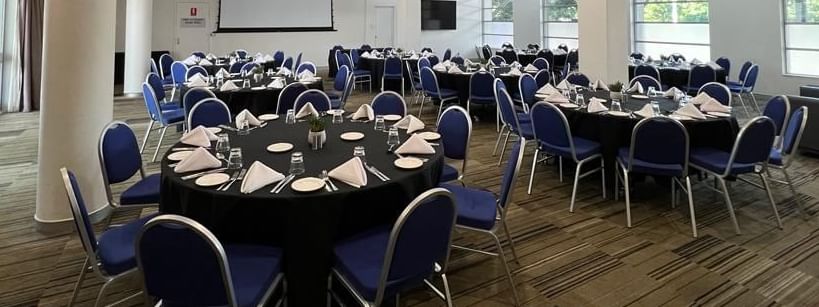 Banquet set-up with projector screen and bright lighting in Parklands Room at Novotel Sydney Olympic Park