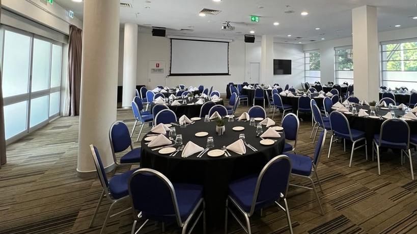 Banquet set-up with projector screen and bright lighting in Parklands Room at Novotel Sydney Olympic Park