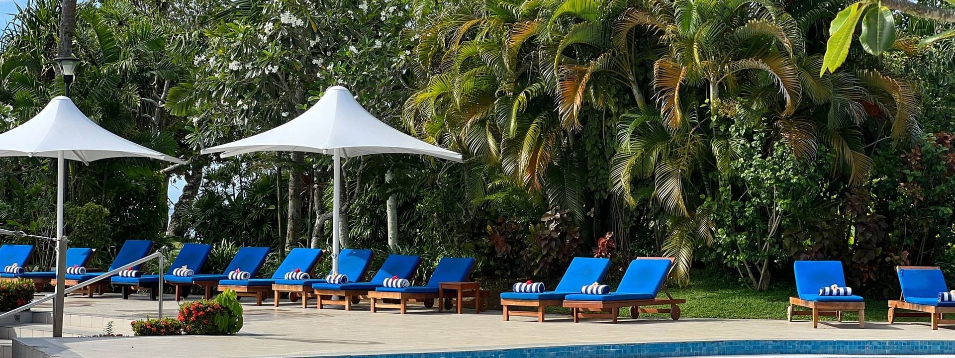 Blue swimming pool with lounge chairs and umbrellas surrounded by lush greenery at The Naviti Resort in Korolevu