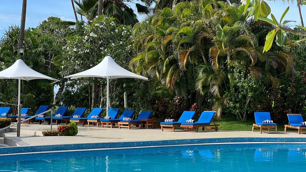 Blue swimming pool with lounge chairs and umbrellas surrounded by lush greenery at The Naviti Resort in Korolevu.