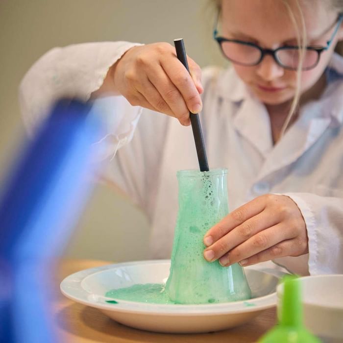 A girl in lab coat stirring green liquid in a glass beaker at Falkensteiner Resort Lake Garda