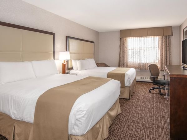 Two beds, nightstands, chair, TV, and window in a hotel room.