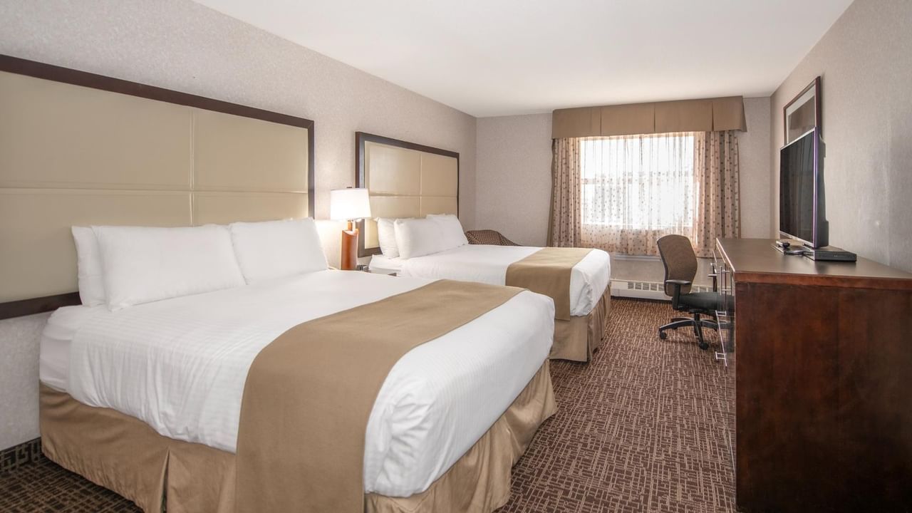 Two beds, nightstands, chair, TV, and window in a hotel room.