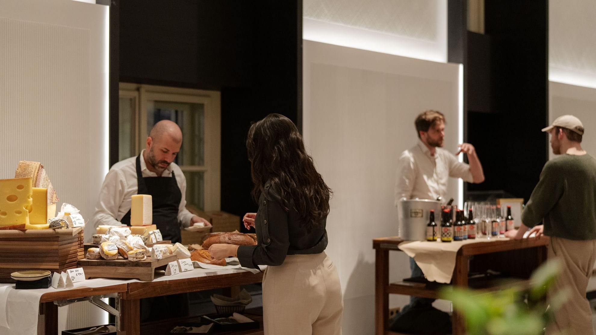 Woman interacting with a vendor in a gourmet food display, featuring an array of cheeses and breads at Almanac Palais Vienna
