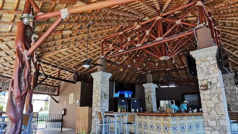 Rustic, open-air bar with a tiled counter under a large thatched roof at Sirenas Restaurant in Hacienda del Mar los Cabos.