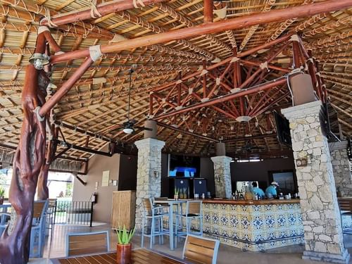 Rustic, open-air bar with a tiled counter under a large thatched roof at Sirenas Restaurant in Hacienda del Mar los Cabos