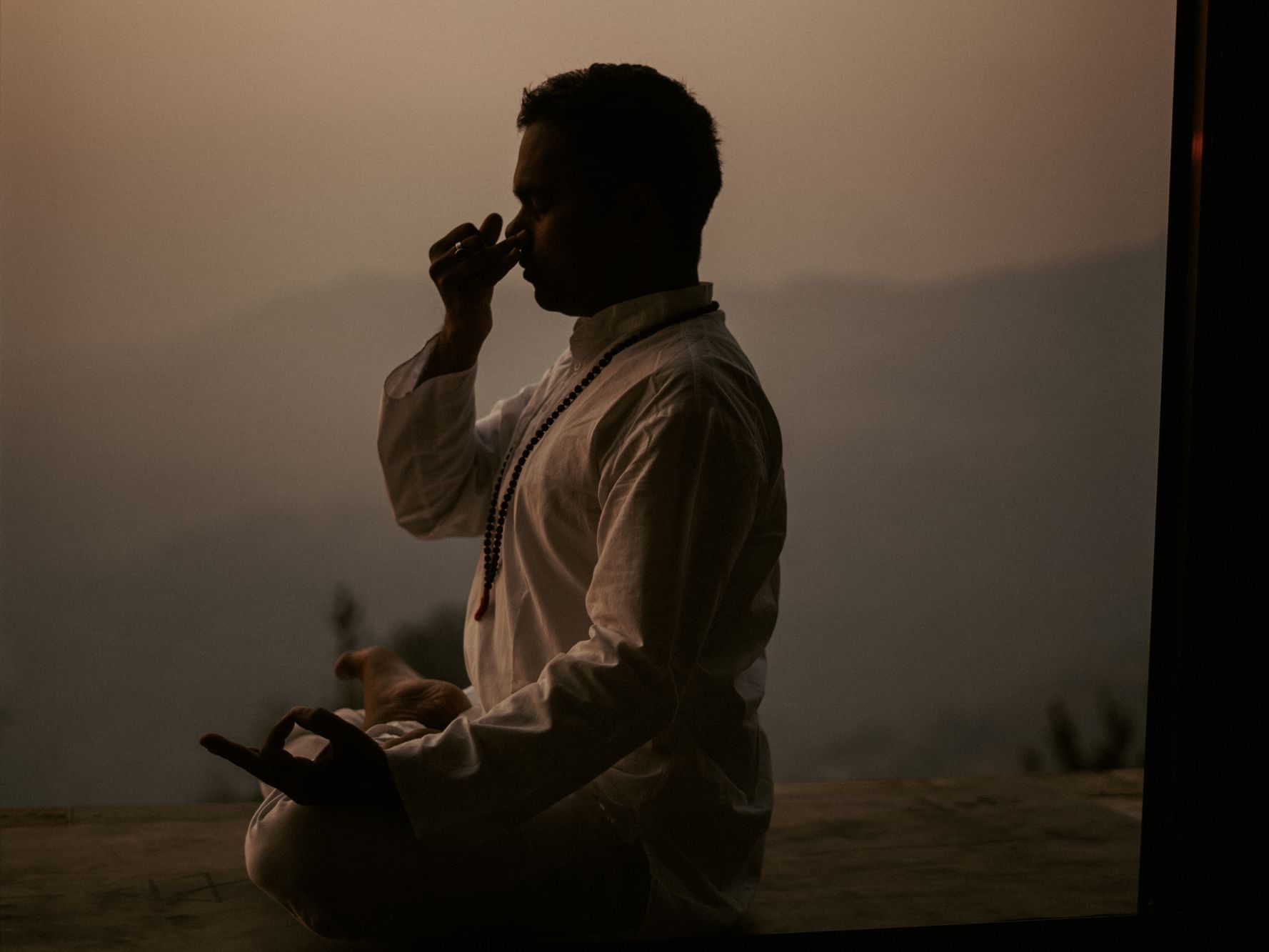 Man meditating in silhouette against a hazy background of mountains at Dwarika's Himalayan Wellbeing