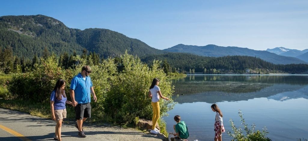 Family walks beside Green Lake in Whistler while enjoying mountain views and a peaceful lakeside path