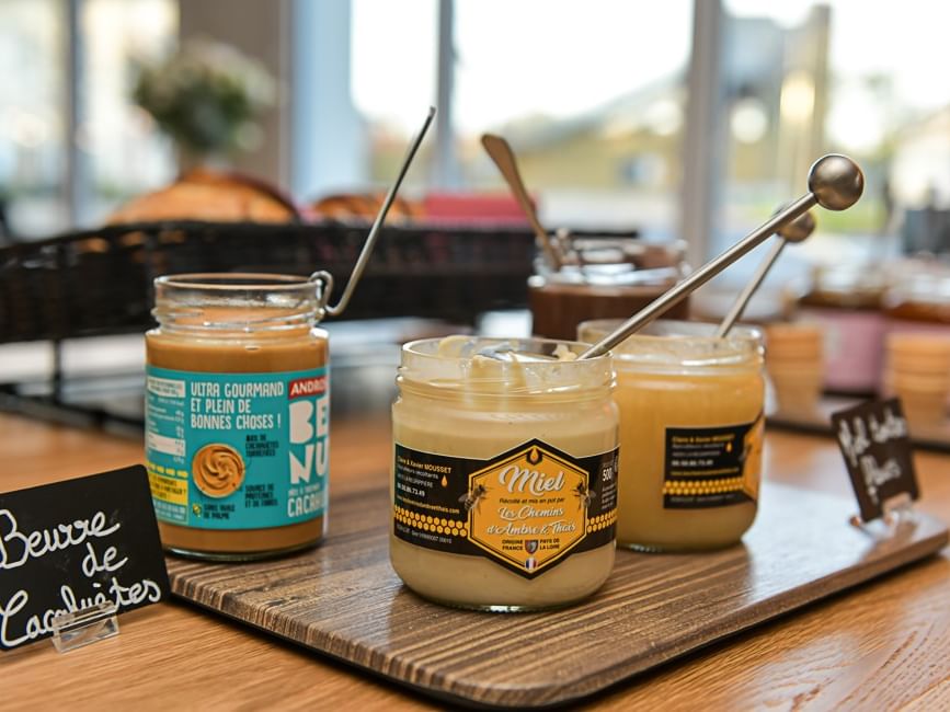 Trois pots de miel ouverts sur planche en bois avec étiquettes à Hôtel Rivella.