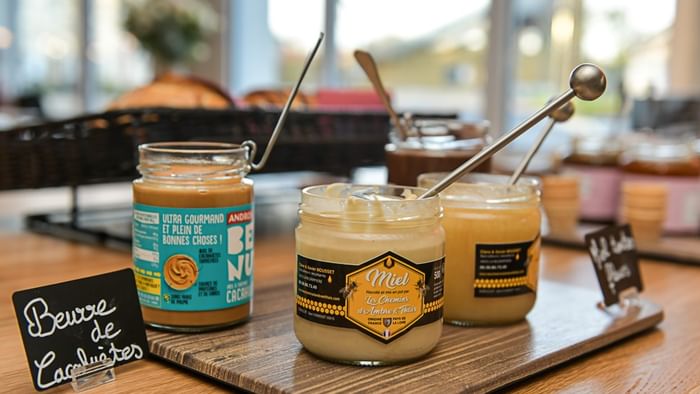 Trois pots de miel ouverts sur planche en bois avec étiquettes à Hôtel Rivella.