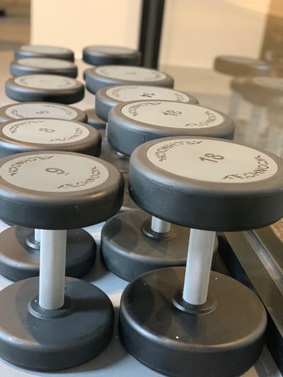 Row of black-rimmed dumbbells, labeled with weights, arranged neatly on a gym rack at Amora Herencia Riverwalk Melbourne