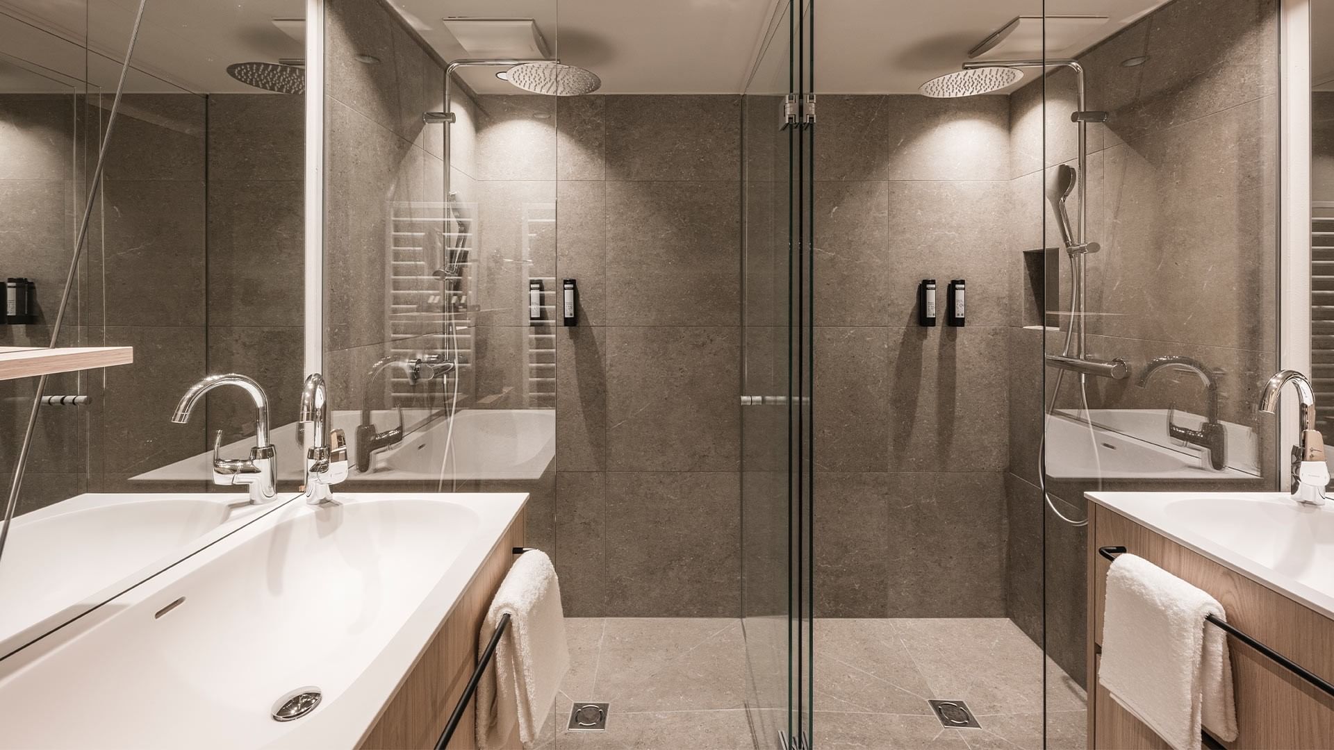 Modernes Badezimmer mit Glasdusche, zwei Waschbecken, und Handtüchern auf Regal.