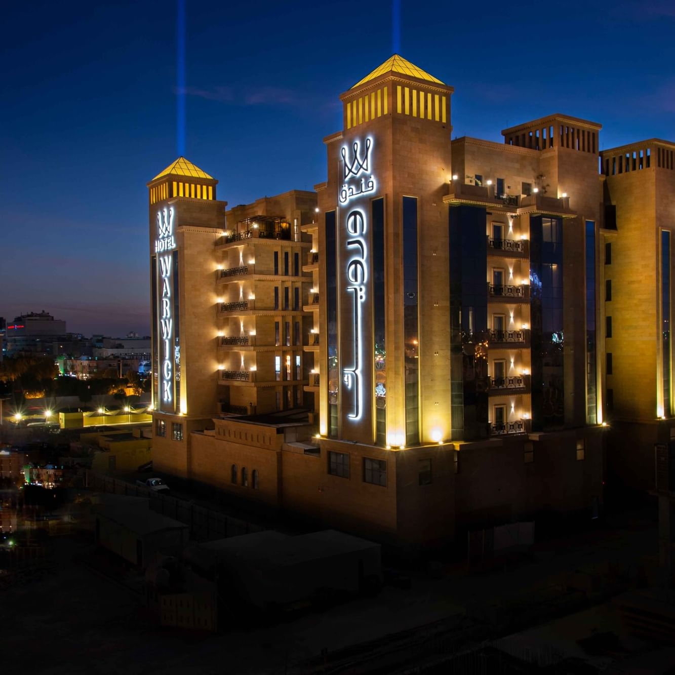 Façade en pierre illuminée du Warwick Al Khobar, avec des inscriptions en arabe lumineuses sous un ciel sombre