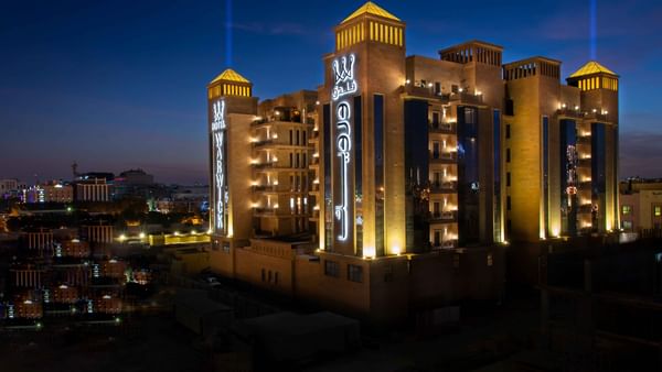 Façade en pierre illuminée du Warwick Al Khobar, avec des inscriptions en arabe lumineuses sous un ciel sombre