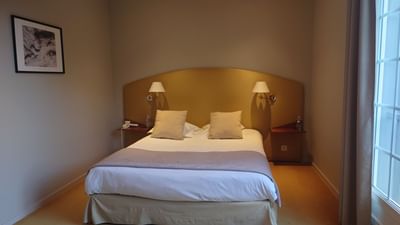 Chambre d'hôtel avec lit double, deux lampes, tableau, deux tables de nuit et une fenêtre.