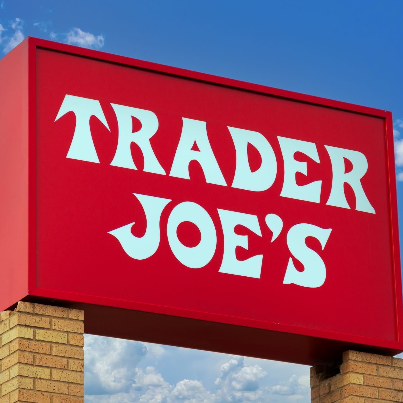 Classic red and white Trader Joe's grocery store sign against a bright blue sky at Tradewinds Apartment Hotel
