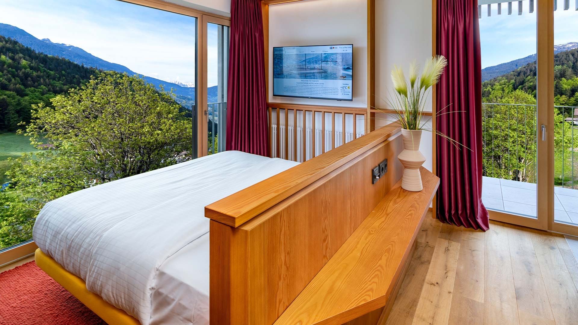 Schlafzimmer mit Holzmöbeln, Fernseher, Balkon und Blick auf die Berge in der Schweiz.