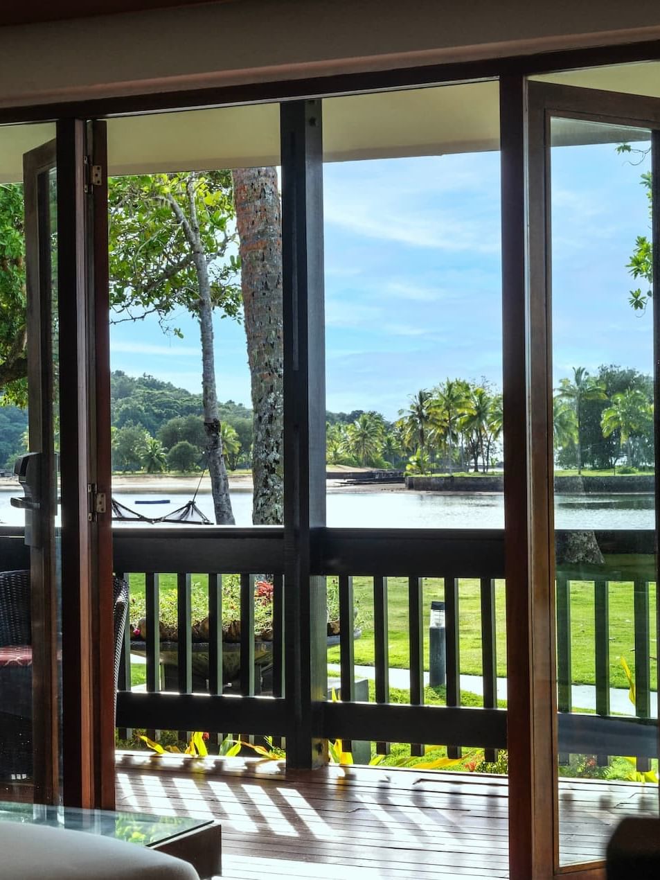 Wicker chairs on a deck by a lawn under palm trees in Studio Villa at The Naviti Resort - Fiji