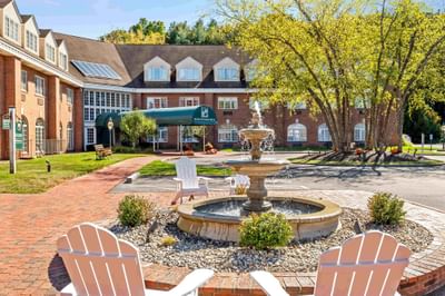 Water fountain with white lawn chairs facing the brick exterior and green entrance awning at Avon Old Farms Hotel