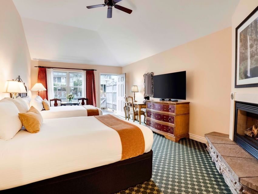 Two beds, fireplace, TV, dresser, chairs, table, ceiling fan, and picture frame in a hotel room.