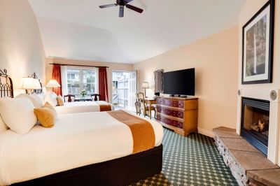 Two beds, fireplace, TV, dresser, chairs, table, ceiling fan, and picture frame in a hotel room.