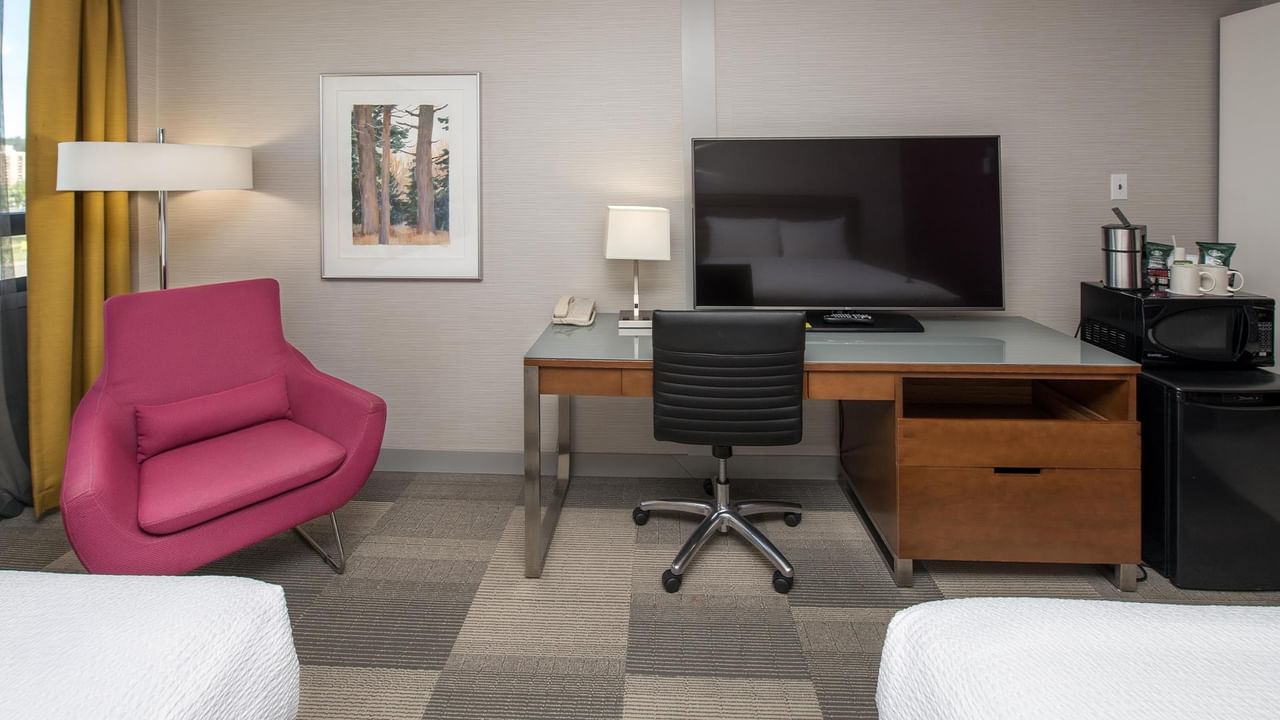 Guest room with work desk, pink accent chair, flat-screen TV, and modern amenities at Coast Prince George Hotel