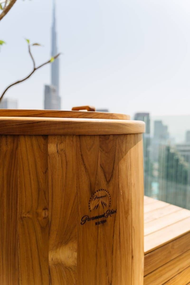 Man relaxing in a refreshing wooden plunge pool on a rooftop at Paramount Hotel Midtown, with a Dubai skyline view