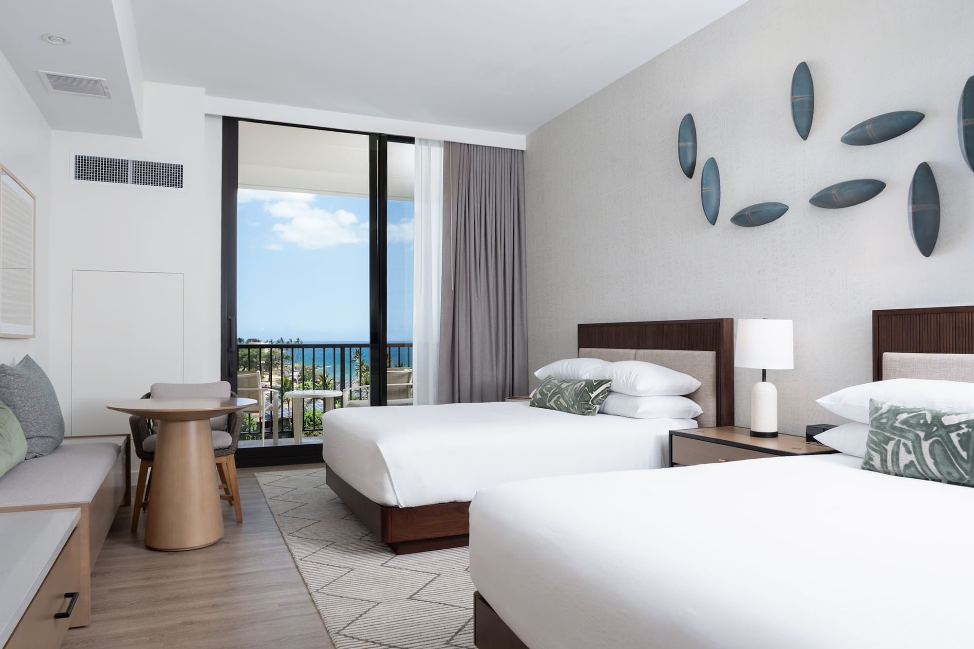 A hotel room with two twin beds, a dining table, a sofa, and a balcony with an ocean view.
