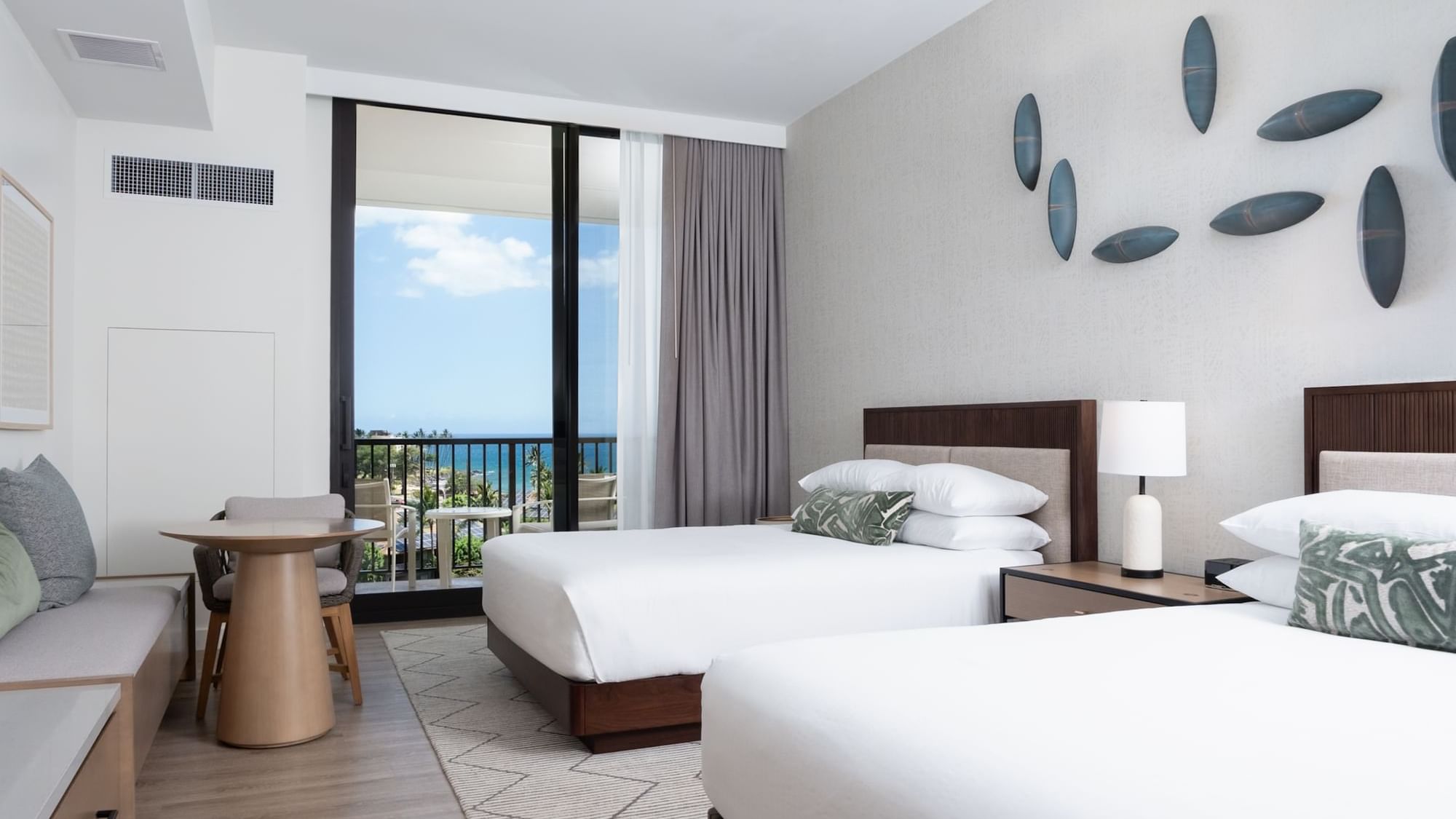 A hotel room with two queen beds, a sofa, a dining table, and a balcony with an ocean view.
