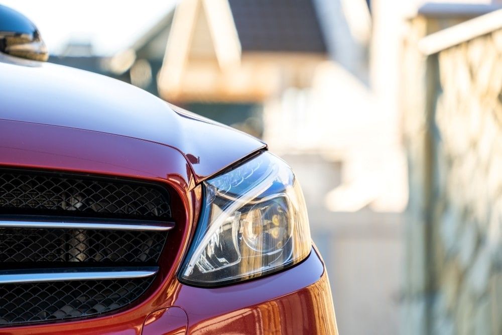 A close-up of a headlight on a red sedan.