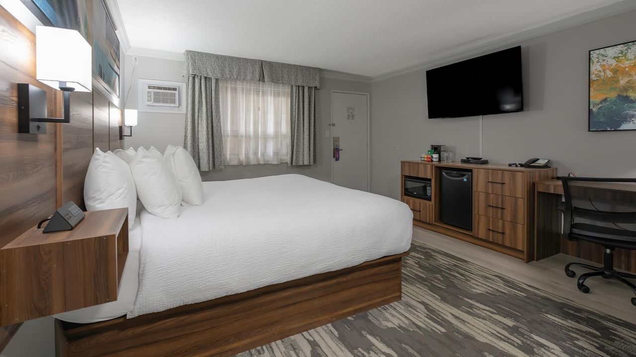 Room with bed, desk, chair, TV, and artwork at Coast Dawson Creek Hotel.