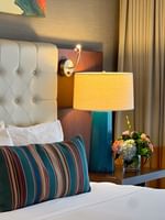 Tufted headboard by a teal lamp and flowers on a wooden nightstand in Magnolia Suite at Warwick Seattle