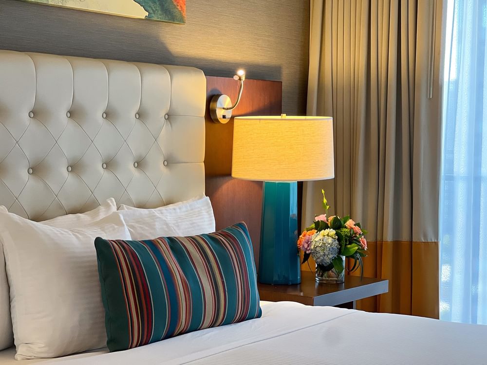 Tufted headboard by a teal lamp and flowers on a wooden nightstand in Magnolia Suite at Warwick Seattle