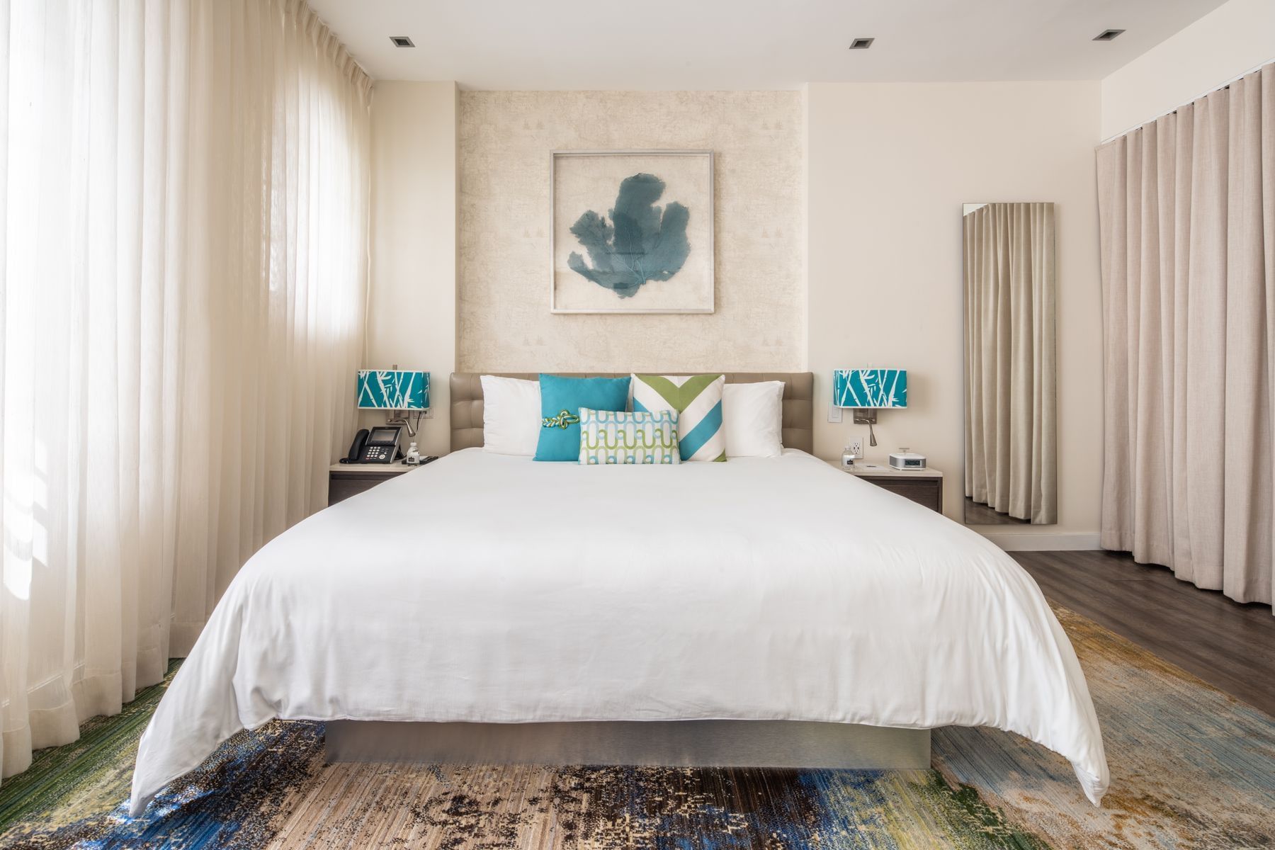A wide view of a hotel room with a large bed, two nightstands, and a painting on the wall.