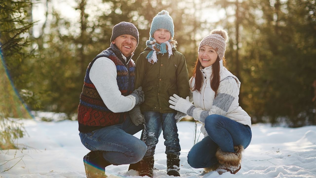 Happy family of three wearing winter clothing kneeling together in snowy forest setting