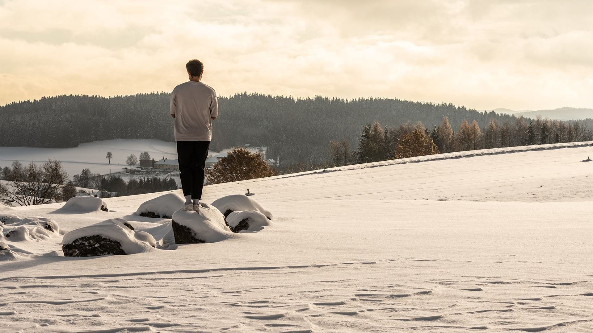 Mann steht auf Felsen in schneebedeckter Landschaft mit Wald im Hintergrund.