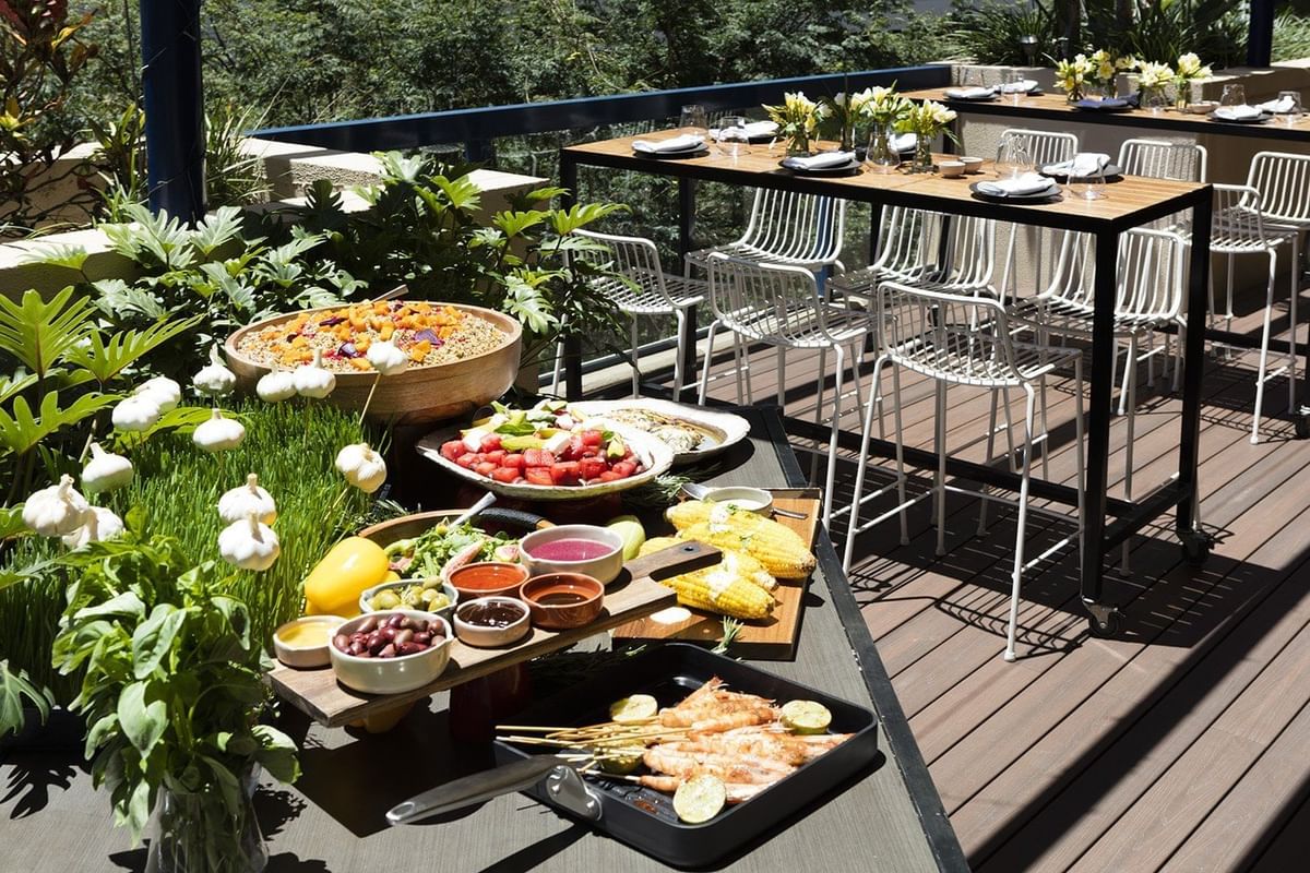 Vibrant outdoor dining deck with fresh salads, grilled corn, and prawns on skewers at The Sebel Brisbane
