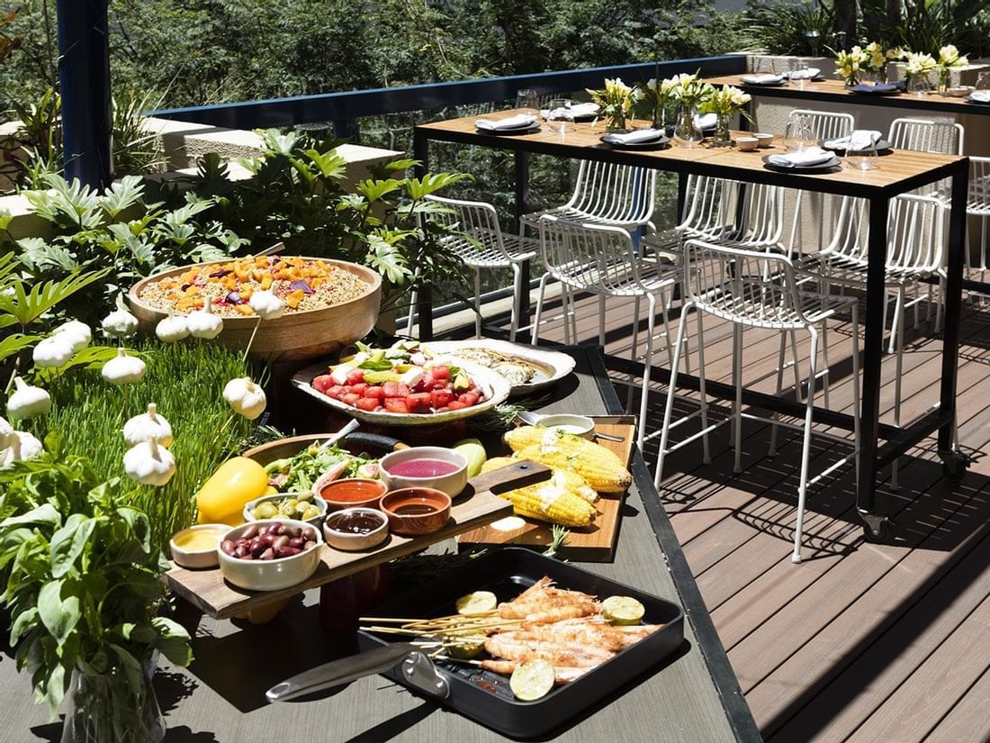 Vibrant outdoor dining deck with fresh salads, grilled corn, and prawns on skewers at The Sebel Brisbane