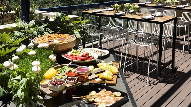Vibrant outdoor dining deck with fresh salads, grilled corn, and prawns on skewers at The Sebel Brisbane