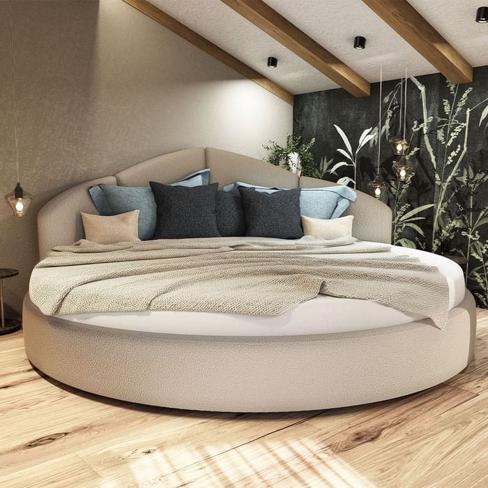 Rundes Bett mit Kissen und Decken, Holzboden, Pflanzen und Hängelampen im Hintergrund.