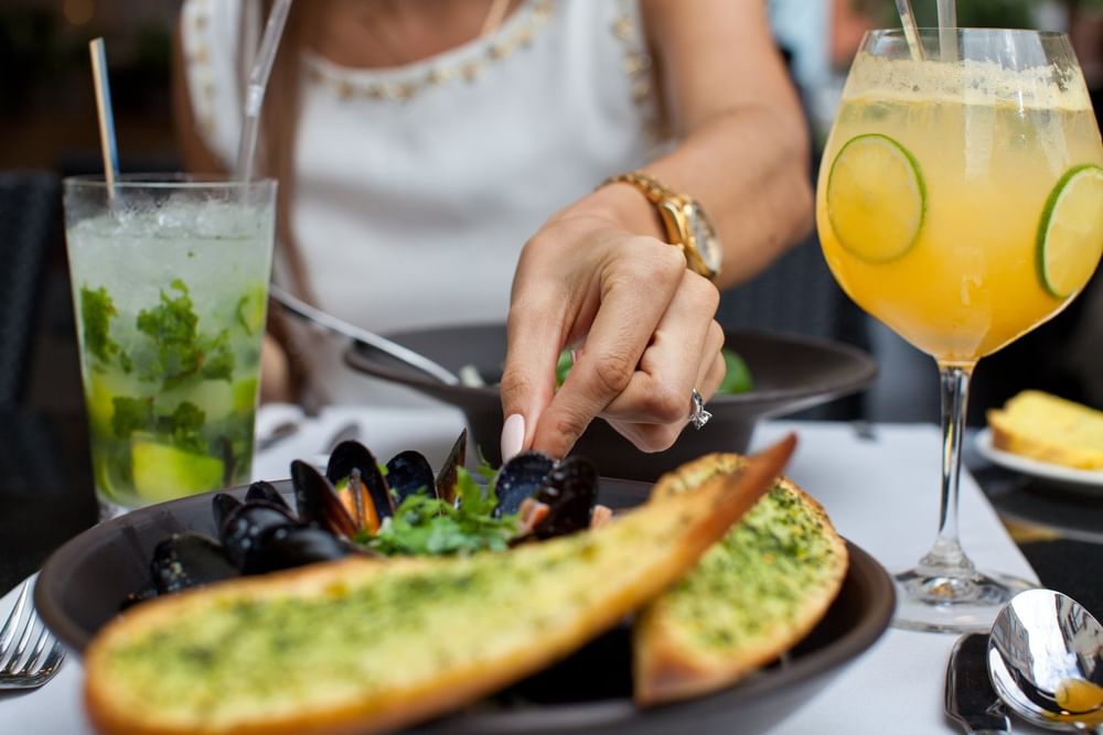 Primer plano de mejillones al vapor con pan de ajo, servidos junto a cócteles tropicales en Fiesta Americana Funeeq